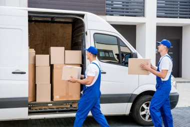 İki nakliye şirketi çalışanı minibüsten yeni eve kutular boşaltıyor.