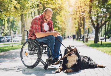 Köpeğiyle birlikte tekerlekli sandalyede fiziksel engelli mutlu bir genç adam..
