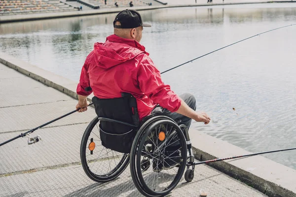 Persona con discapacidad física en una silla de ruedas que pesca desde el muelle de pesca. — Foto de Stock