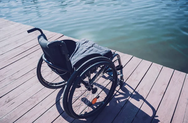 Tekerlekli sandalyesi iskelede beklerken fiziksel engelli bir adam nehirde yüzüyor.