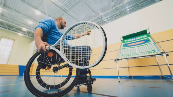 Dospělý muž s tělesným postižením, který používá invalidní vozík hraje tenis na krytém tenisovém kurtu — Stock fotografie