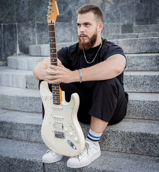 Νεαρός μουσικός του δρόμου παίζει κιθάρα κάθεται σε γρανίτη βήματα — Φωτογραφία Αρχείου