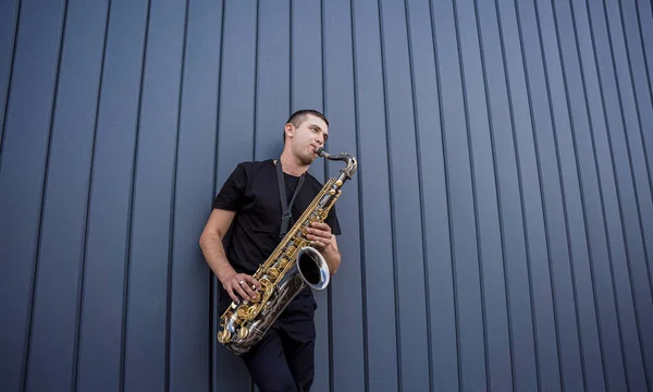 Joven músico callejero tocando el saxofón cerca de la gran pared azul — Foto de Stock