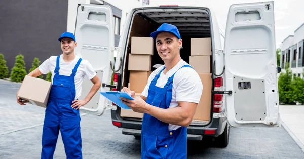 Dos trabajadores de la empresa de mudanzas descargan cajas de minibús en el hogar de los clientes —  Fotos de Stock