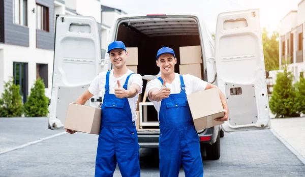 Dos trabajadores de la empresa de mudanzas descargan cajas de minibús en el hogar de los clientes —  Fotos de Stock