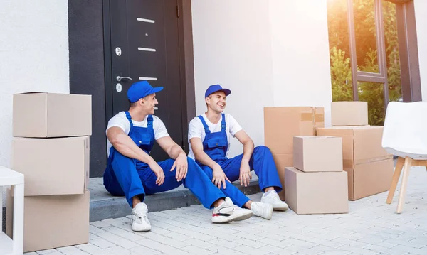 İki nakliye şirketi çalışanı merdivende otururken mola veriyor.