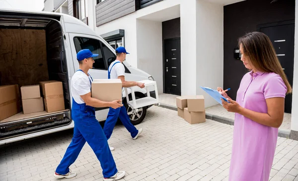 İki nakliye şirketi çalışanı minibüsten müşterilerin evlerine kutu indiriyor.