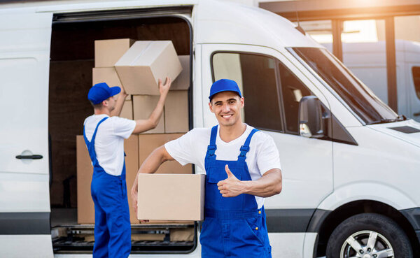Two removal company workers unloading boxes from minibus into new home