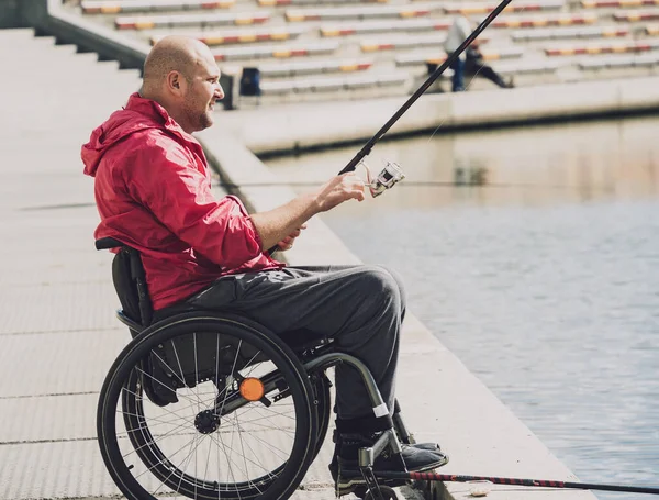 Persona con discapacidad física que utiliza la pesca en silla de ruedas desde el muelle de pesca. — Foto de Stock