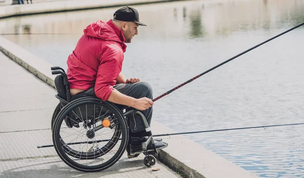 Persona con discapacidad física que utiliza la pesca en silla de ruedas desde el muelle de pesca. — Foto de Stock