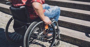 Merdivenlerin önünde tekerlekli sandalye kullanan fiziksel engelli genç bir adam.