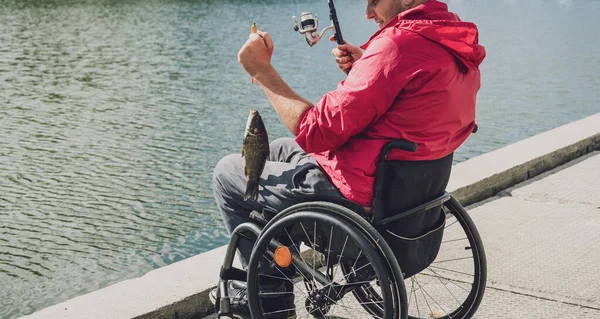 Persona con discapacidad física que utiliza la pesca en silla de ruedas desde el muelle de pesca. — Foto de Stock