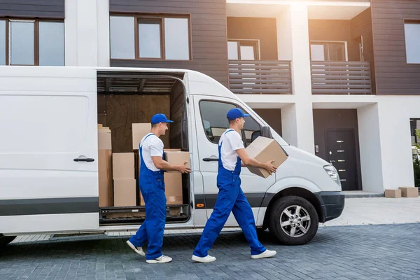 Dos trabajadores de la empresa de mudanzas descargan cajas de minibús en un nuevo hogar — Foto de Stock