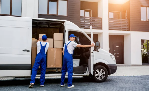 Dos trabajadores de la empresa de mudanzas descargan cajas de minibús en un nuevo hogar —  Fotos de Stock