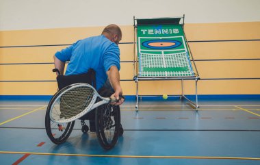 Tekerlekli sandalyeyle tenis oynayan fiziksel engelli yetişkin bir adam.