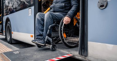 Fiziksel engelli kişiler toplu taşımadan erişilebilir bir rampayla çıkıyorlar..