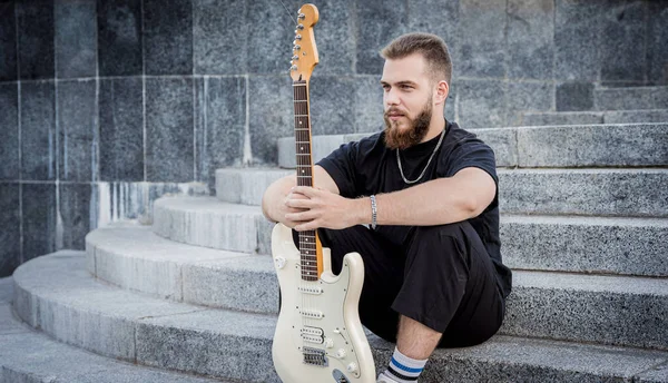 Jovem músico de rua tocando guitarra sentado em degraus de granito — Fotografia de Stock