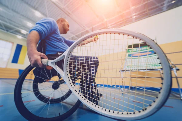 Dorosły mężczyzna z niepełnosprawnością fizyczną, który używa wózka inwalidzkiego do gry w tenisa na krytym korcie tenisowym — Zdjęcie stockowe
