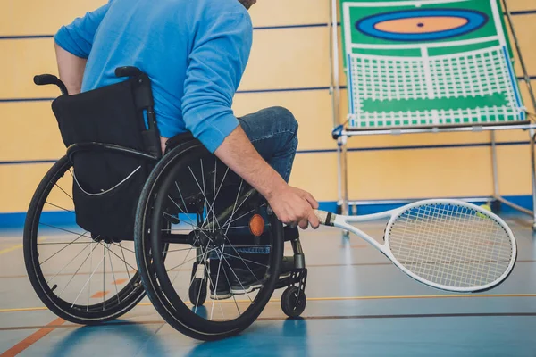 Взрослый человек с ограниченными физическими возможностями, который использует инвалидное кресло, играя в теннис на крытом теннисном корте — стоковое фото