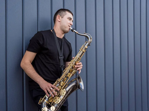 Jeune musicien de rue jouant du saxophone près du grand mur bleu — Photo