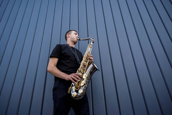 Joven músico callejero tocando el saxofón cerca de la gran pared azul — Foto de Stock