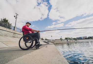 Balıkçı iskelesinden tekerlekli sandalyede balık tutan fiziksel engelli biri..