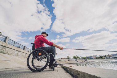 Balıkçı iskelesinden tekerlekli sandalyede balık tutan fiziksel engelli biri..
