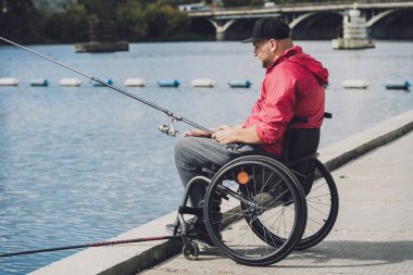 Balıkçı iskelesinden tekerlekli sandalyede balık tutan fiziksel engelli biri..