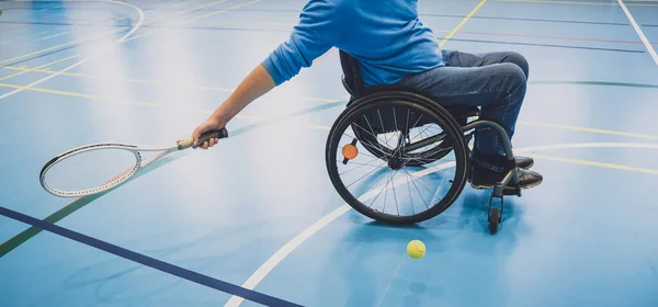 Fyysisesti vammainen aikuinen mies, joka pelaa tennistä sisätenniskentällä pyörätuolilla — kuvapankkivalokuva
