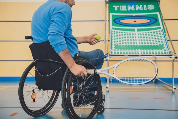 Adult man with a physical disability who uses wheelchair playing tennis on indoor tennis court — Stock Photo, Image