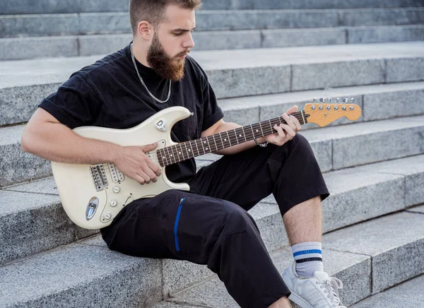 Joven músico callejero tocando la guitarra sentado en escalones de granito — Foto de Stock