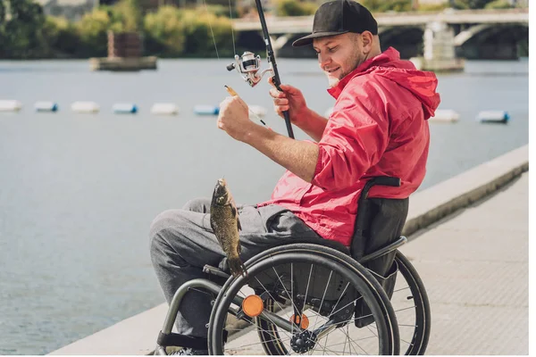 Liikuntarajoitteinen henkilö, joka kalastaa pyörätuolilla kalastuslaiturilta. — kuvapankkivalokuva