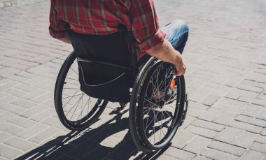 Sokakta tekerlekli sandalyeyle yürüyen fiziksel engelli bir genç.