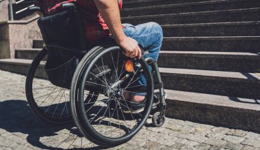 Merdivenlerin önünde tekerlekli sandalye kullanan fiziksel engelli genç bir adam.