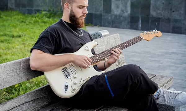 Νεαρός μουσικός του δρόμου που παίζει κιθάρα ενώ κάθεται στον πάγκο — Φωτογραφία Αρχείου