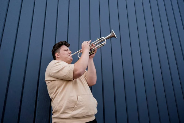 Joven músico callejero tocando la trompeta cerca de la gran pared azul — Foto de Stock