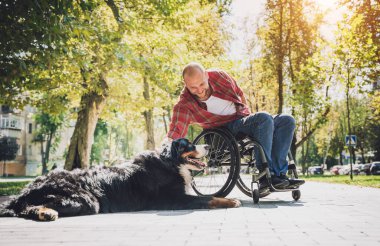 Köpeğiyle tekerlekli sandalye kullanan fiziksel engelli genç adam..