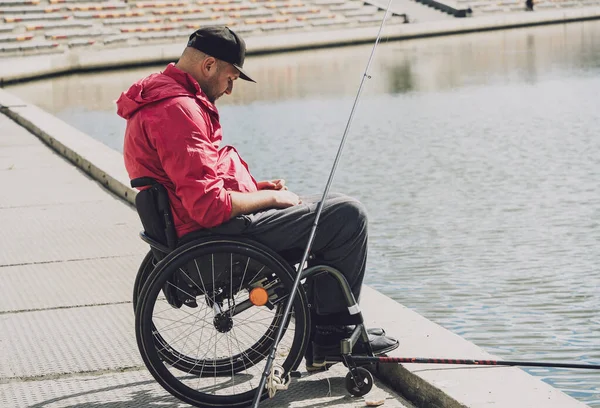 Persona con discapacidad física que utiliza la pesca en silla de ruedas desde el muelle de pesca. — Foto de Stock