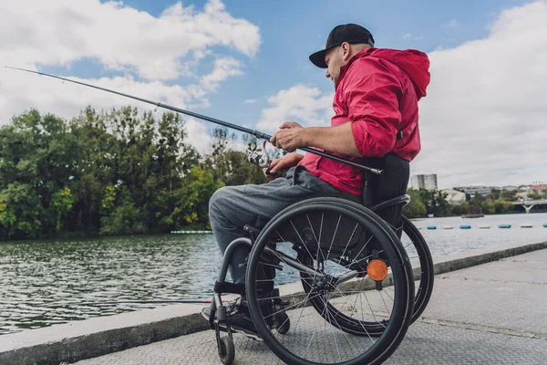 Persona con discapacidad física que utiliza la pesca en silla de ruedas desde el muelle de pesca. — Foto de Stock