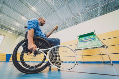 Tekerlekli sandalyeyle tenis oynayan fiziksel engelli yetişkin bir adam.