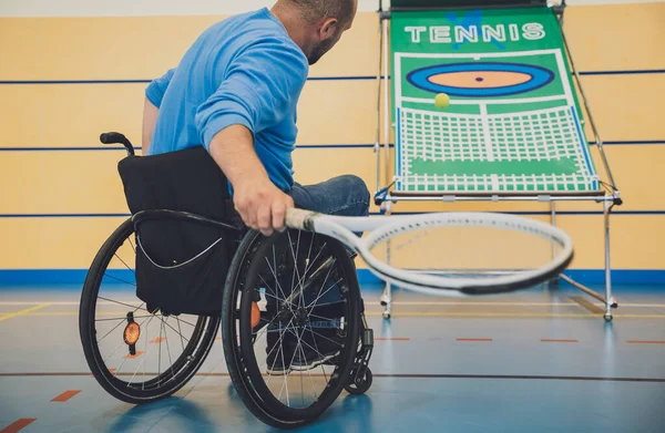 Homme adulte ayant un handicap physique qui utilise un fauteuil roulant pour jouer au tennis sur un court de tennis intérieur — Photo