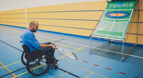Erwachsener Mann mit körperlicher Behinderung, der Rollstuhl benutzt, um Tennis auf dem Tennisplatz zu spielen — Stockfoto