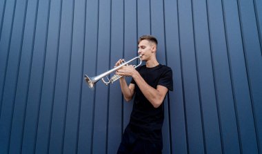 Büyük mavi duvarın yanında trompet çalan genç bir sokak müzisyeni.