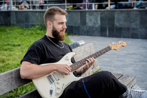 Young street musician playing guitar while sitting on the bench — 图库照片