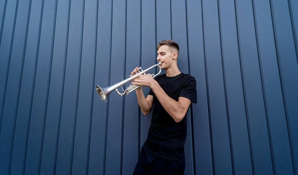 Young street musician playing the trumpet near the big blue wall — Stock Photo, Image