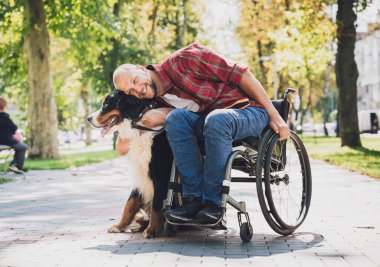 Köpeğiyle tekerlekli sandalye kullanan fiziksel engelli genç adam..
