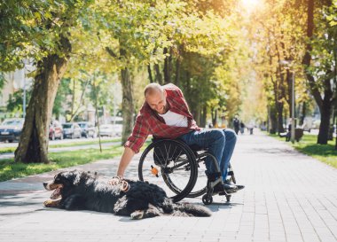 Köpeğiyle tekerlekli sandalye kullanan fiziksel engelli genç adam..