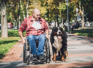 Köpeğiyle tekerlekli sandalye kullanan fiziksel engelli genç adam..
