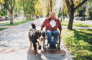 Köpeğiyle tekerlekli sandalye kullanan fiziksel engelli genç adam..