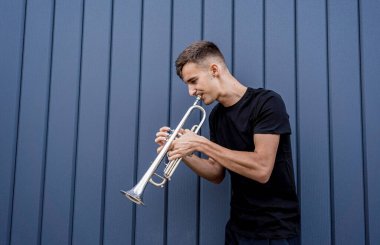 Büyük mavi duvarın yanında trompet çalan genç bir sokak müzisyeni.